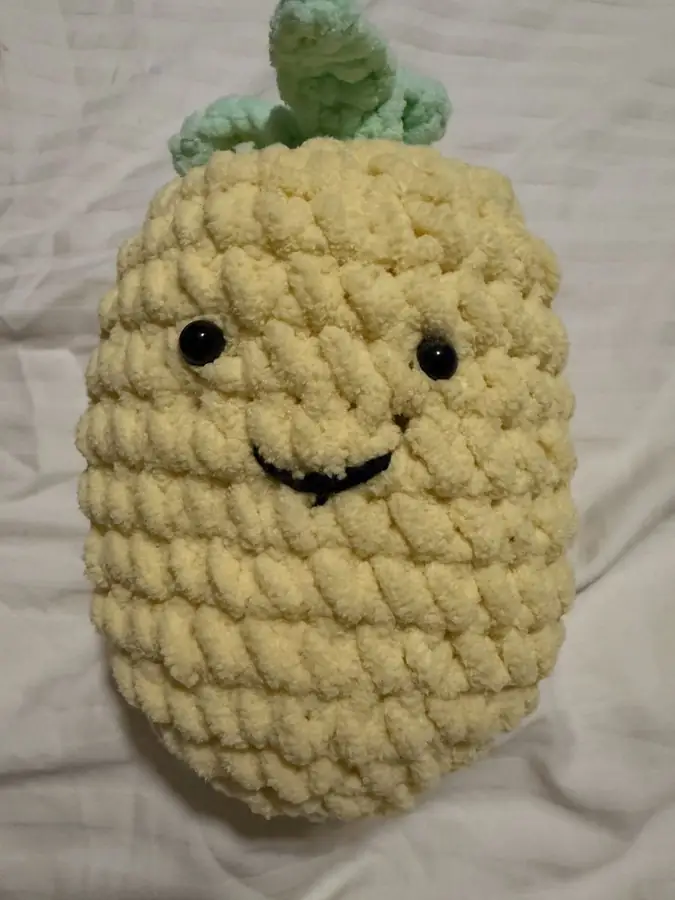 A yellow crochet pineapple with a green leafy top and a smile.