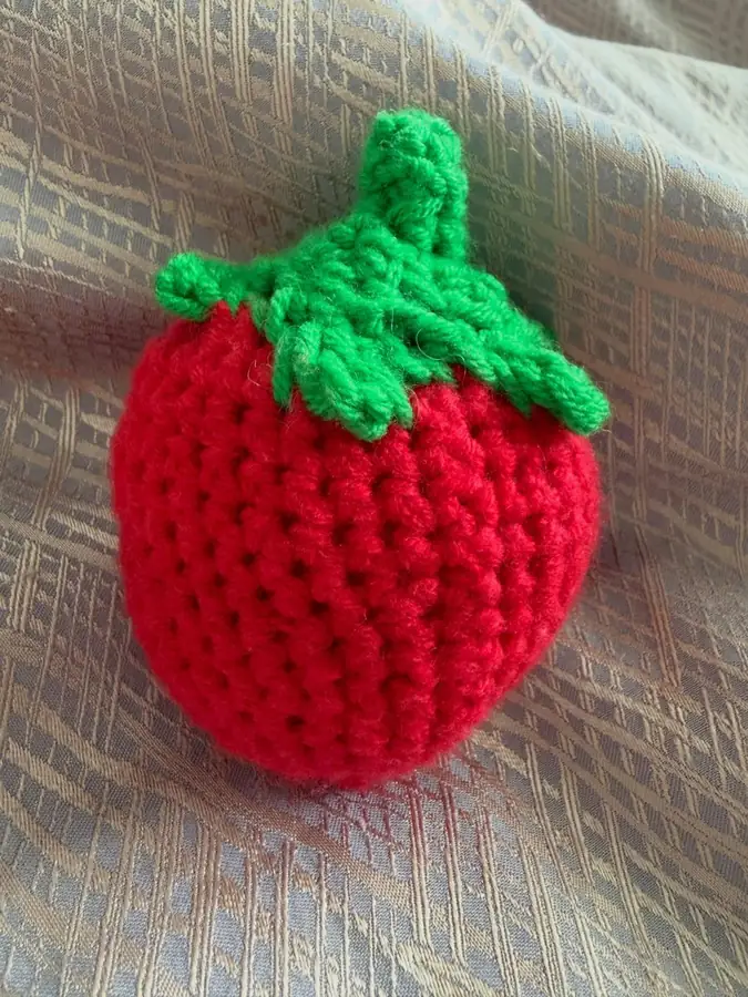 A red crochet strawberry with a green leafy top.