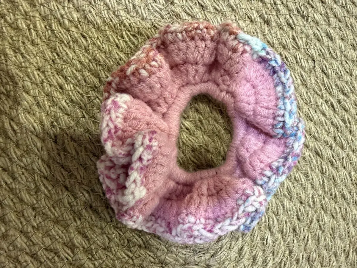 A handmade ruffle scrunchie in pink with a blue confetti edge.