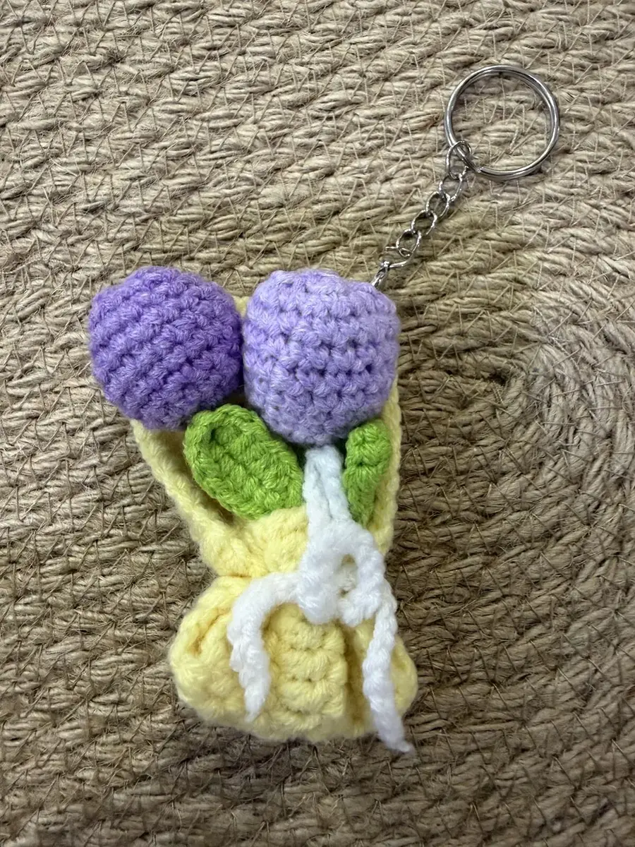 A mini crochet purple flower bouquet keychain with a yellow wrap.