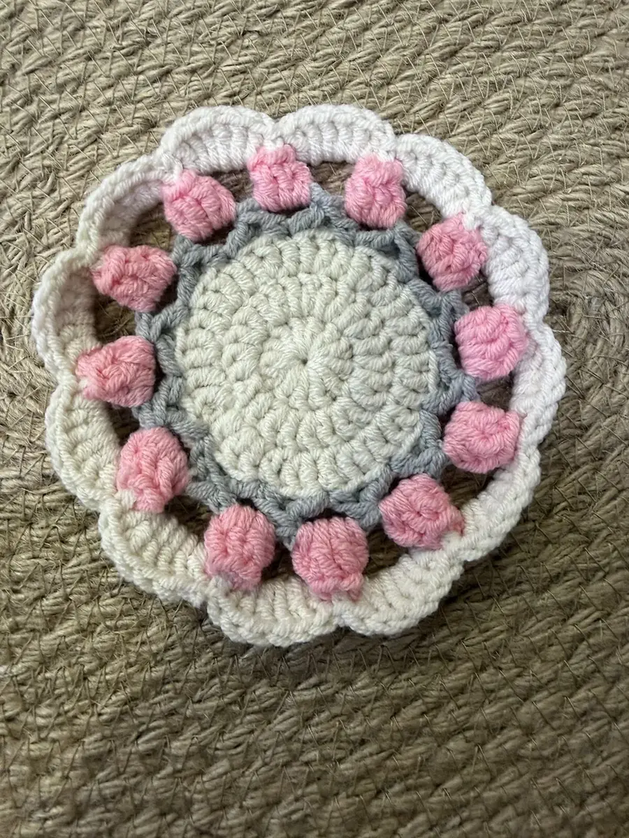 A flower coaster with pink puffs.