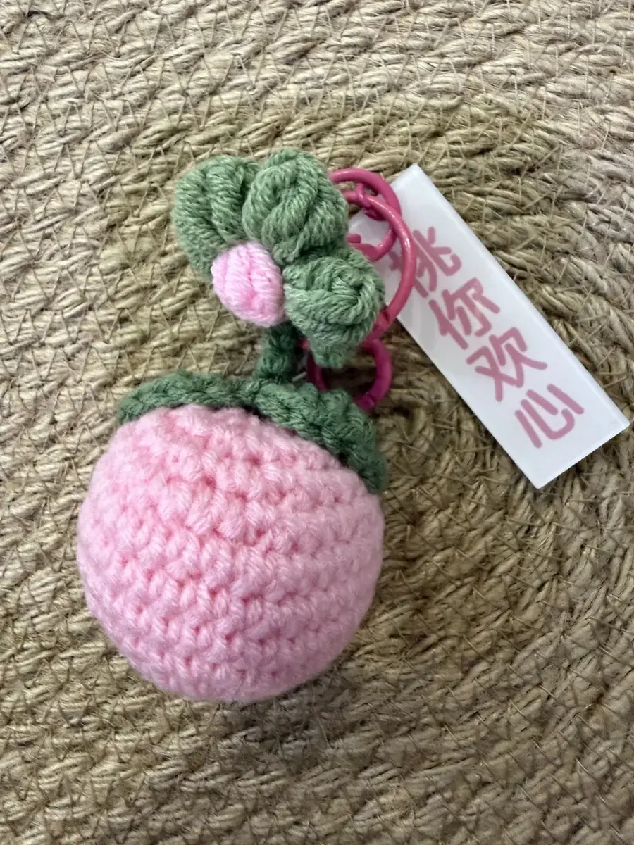 A pink crochet fruit keychain with a green leafy top.