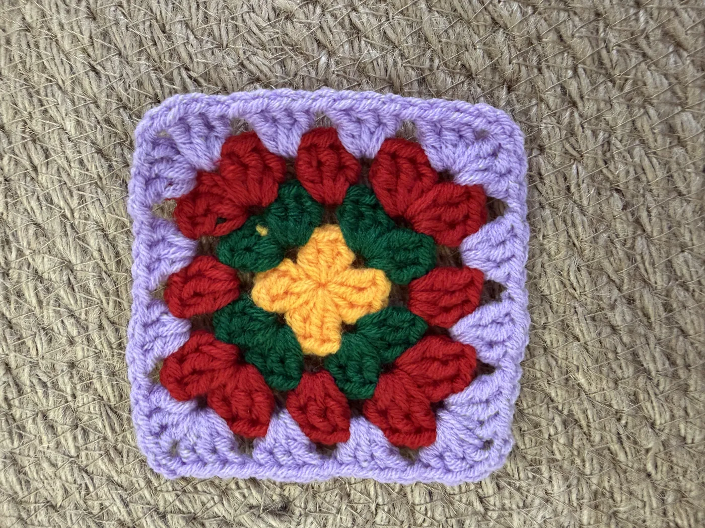 A crochet granny square in purple, red and yellow.