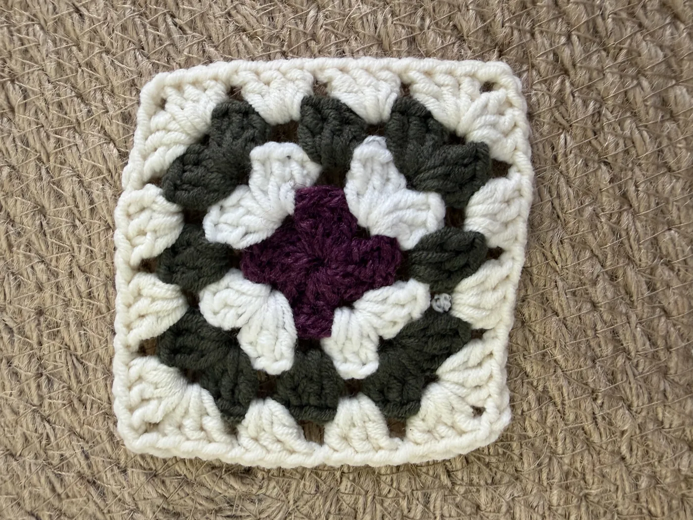 A crochet granny square in black, white and plum.